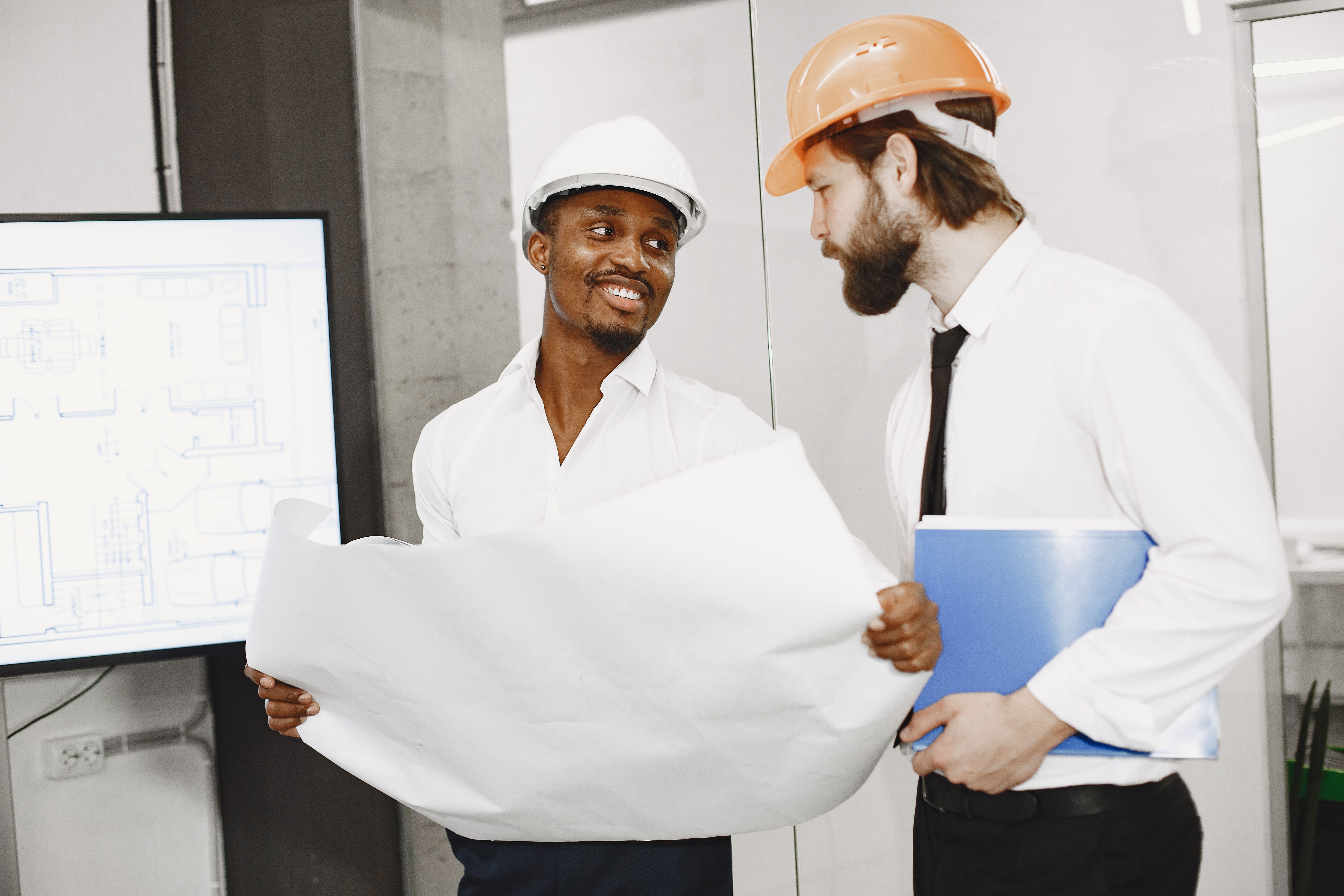 Two architects in hard hats discussing blueprints in a modern office