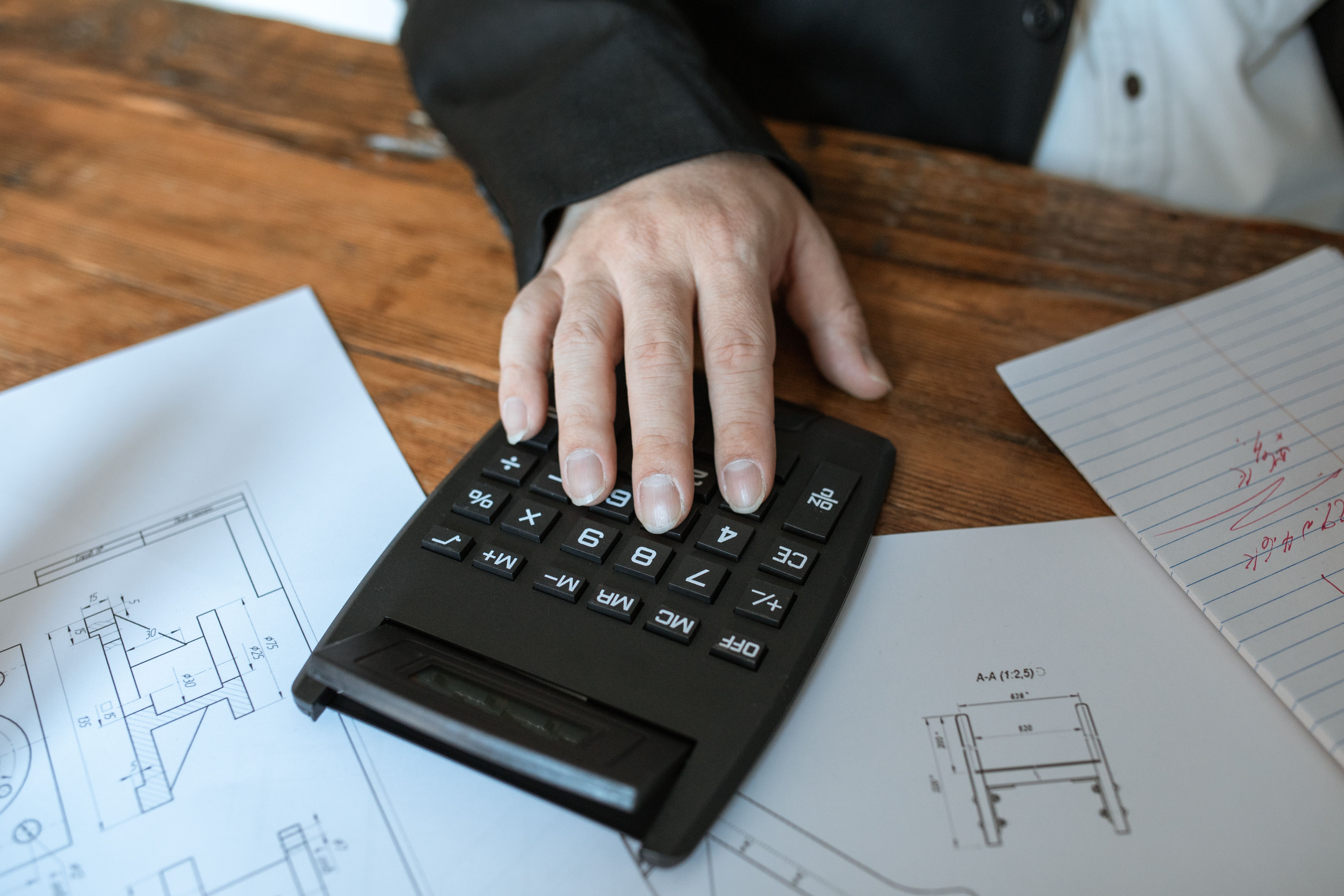 Hand using a calculator for architectural cost calculations on blueprints
