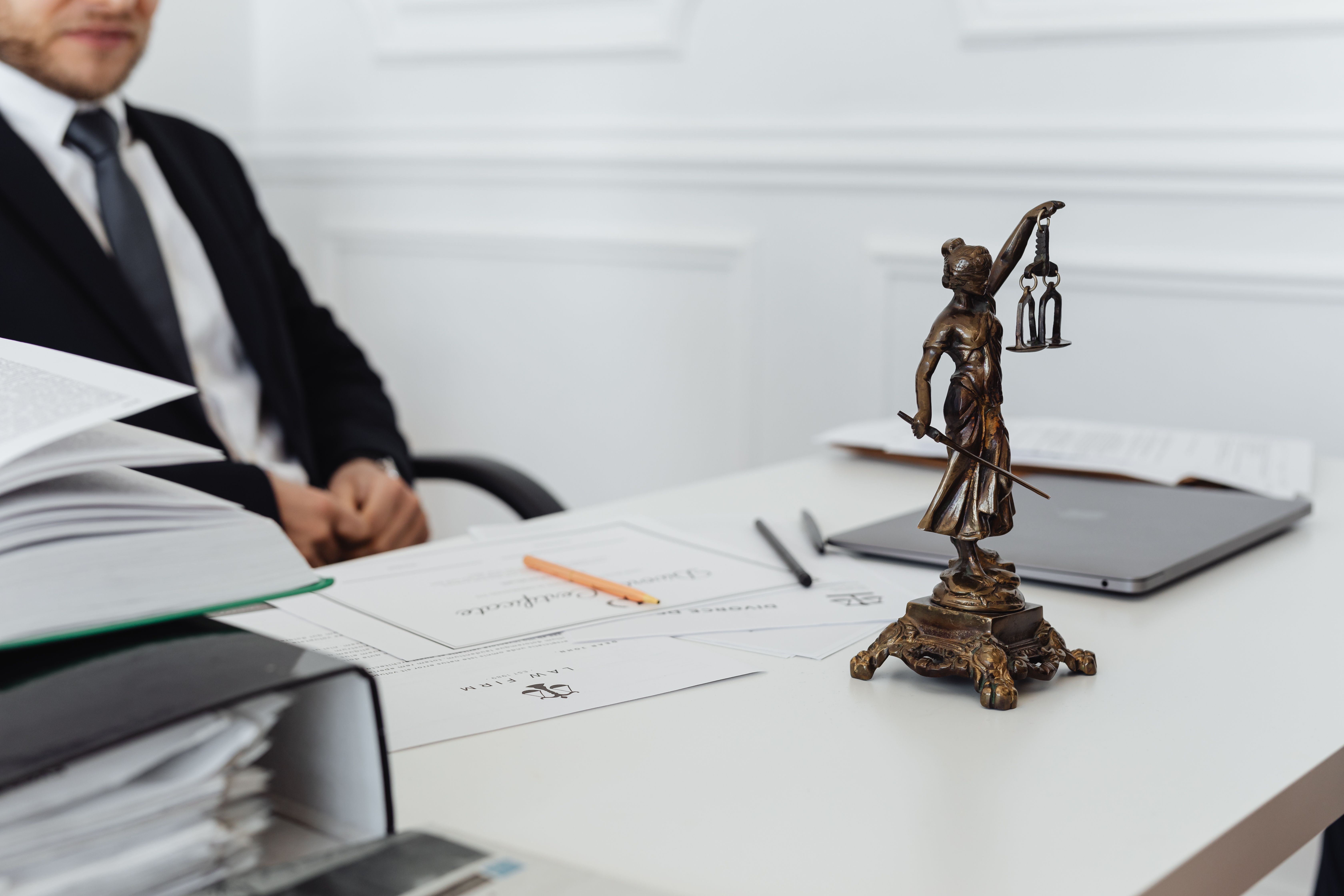 A legal professional's workspace featuring a Lady Justice statue, documents, and a laptop