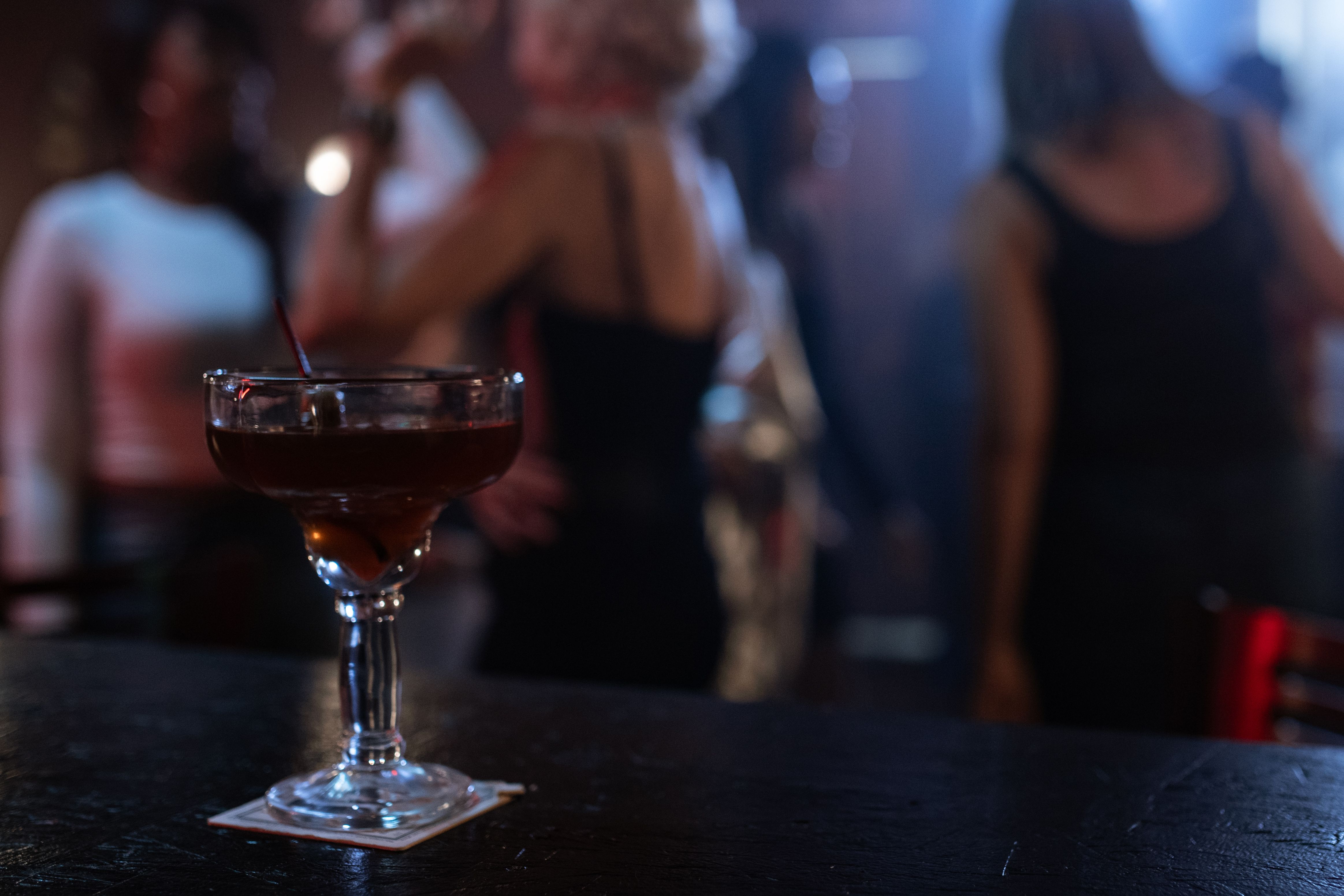A cocktail in focus against a blurred, lively nightclub atmosphere.